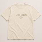 An off-white short-sleeve crewneck t-shirt with 'Loved properly.' and two interlocking ring symbols printed in brown on the chest, displayed flat against a light beige background.