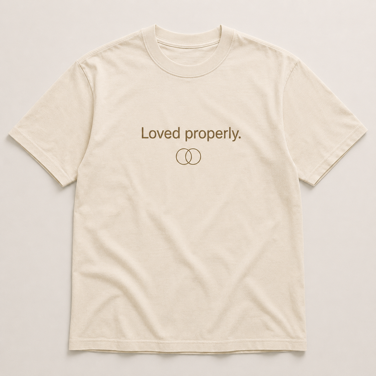An off-white short-sleeve crewneck t-shirt with 'Loved properly.' and two interlocking ring symbols printed in brown on the chest, displayed flat against a light beige background.