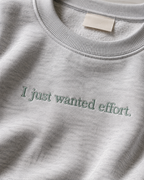 Folded Heather Gray crewneck sweatshirt with dark embroidery reading “I just wanted effort.” on a light background.