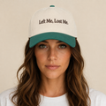 A woman wearing a baseball cap with the embroidered text 'Left Me, Lost Me.' in black on an off-white crown and a teal-green visor and top button, against a plain beige background.