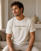 Warm cream T-shirt with camel brown text reading “Loved properly.” above two interlocking circles.