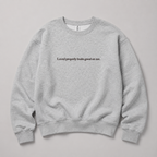 A light heather gray crewneck sweatshirt with the black printed text 'Loved properly looks good on me.' across the chest, displayed flat against a neutral gray background.