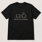 A black short-sleeve crewneck t-shirt with a white graphic of two coffee cups and the text 'Still miss you sometimes.' printed on the chest, displayed flat against a light beige background.